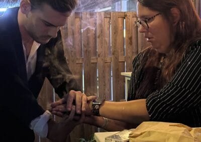 Goochelaar voert een close-up truc uit met de hand van een toeschouwer aan een tafel tijdens een event, terwijl zij aandachtig meekijkt.