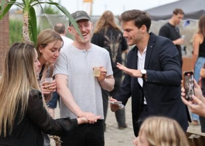 Goochelaar voert een interactieve kaarttruc uit voor een groepje mensen tijdens een buitenevent, terwijl ze nieuwsgierig en enthousiast toekijken.