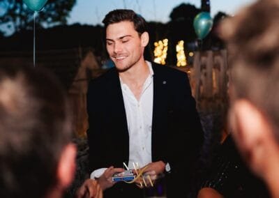 Goochelaar voert een close-up truc uit met lucifers en speelkaarten terwijl gasten toekijken tijdens een sfeervol avondfeest.